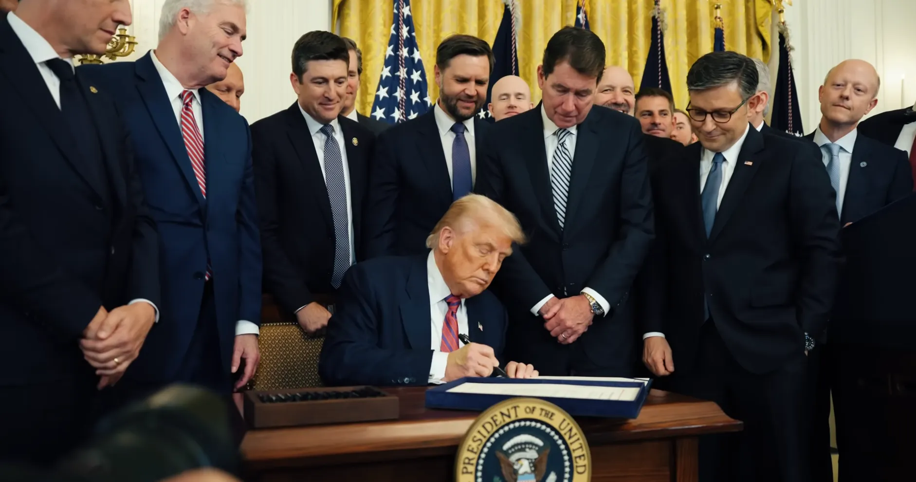 Impresión de pantalla de un video oficial de la casa blanca donde se ve a donald trump firmando la lay de regulación de la stablecoins, acompañado por el vicepresidente JD Vance y otros republicanos